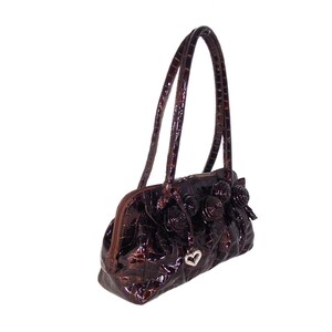 Pu&ograve; includere: Una borsa a mano marrone con stampa coccodrillo, un ciondolo a forma di cuore e decorazioni floreali.