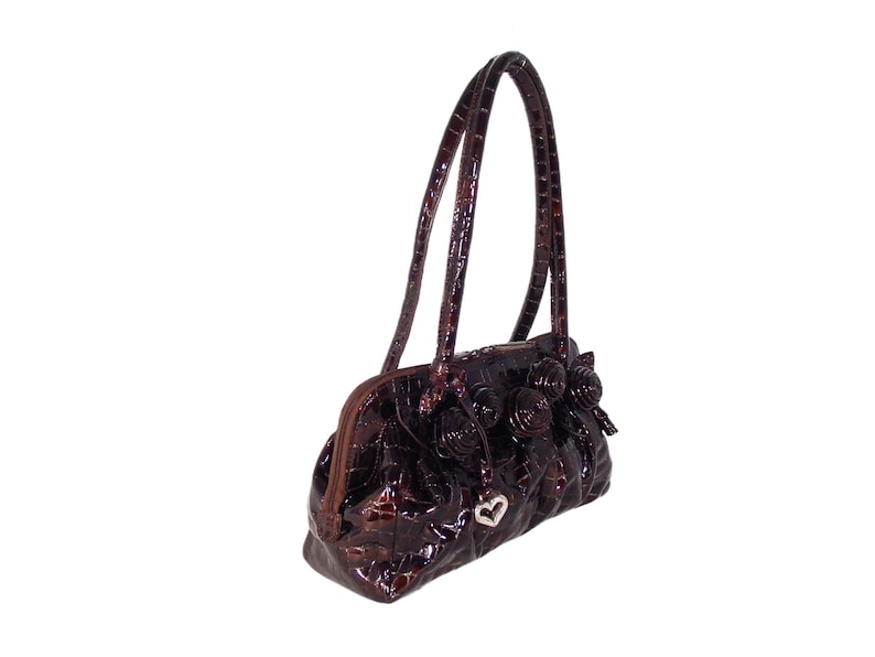 Pu&ograve; includere: Una borsa a mano marrone con stampa coccodrillo, un ciondolo a forma di cuore e decorazioni floreali.