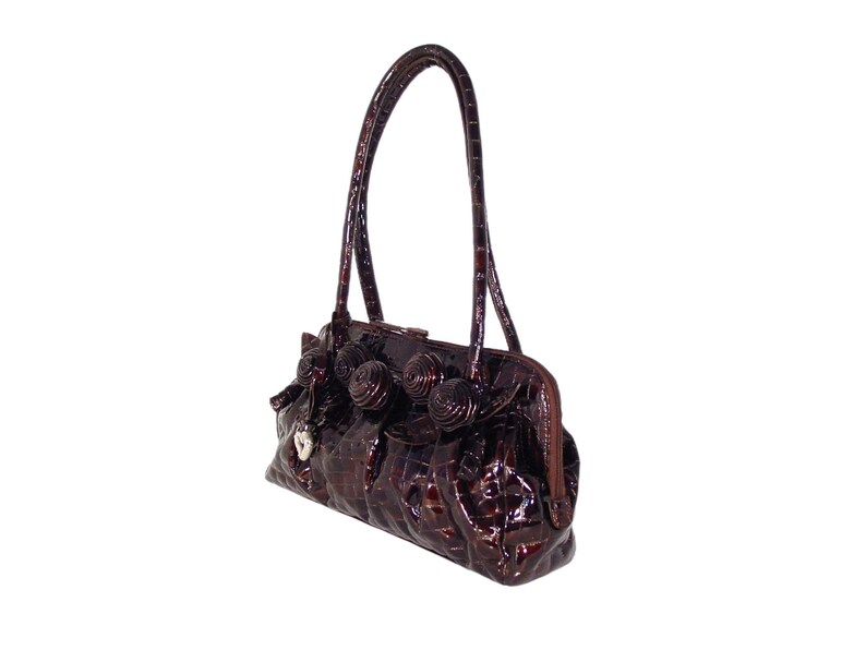 Pu&ograve; includere: Una borsa a mano in pelle marrone con effetto coccodrilo, con un design floreale decorativo e un ciondolo a forma di cuore argentato.