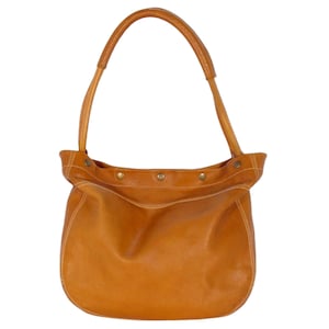 May include: A tan leather tote bag with a single strap. The bag has a rounded bottom and a flap closure with multiple button accents.