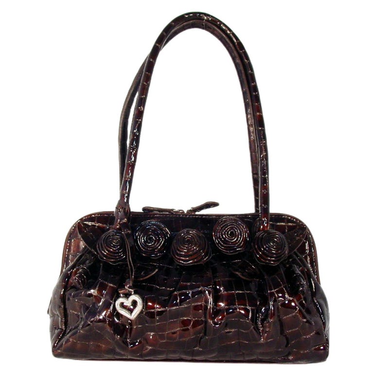 Pu&ograve; includere: Una borsa a mano in pelle marrone con effetto coccodrillo, con un ciondolo a forma di cuore e rosette decorative sul davanti.