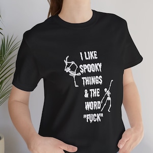 May include: Black t-shirt with a white graphic of two skeletons dancing and the text "I like spooky things & the word "F*CK""