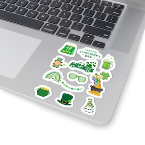 Könnte beinhalten: Ein Set mit 12 St. Patricks Day-Aufklebern mit verschiedenen Designs in Grün und Gold, darunter ein Kobold, ein Topf mit Gold, ein Regenbogen, ein Kleeblatt, ein Bierkrug und ein LKW. Die Aufkleber sind auf weißem Papier gedruckt und haben eine glänzende Oberfläche.