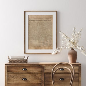 May include: A framed print of the Declaration of Independence, with the text "In CONGRESS, July 4, 1776. The unanimous Declaration of the thirteen united States of America." The print is hanging on a white wall above a wooden dresser with a wicker basket on top.