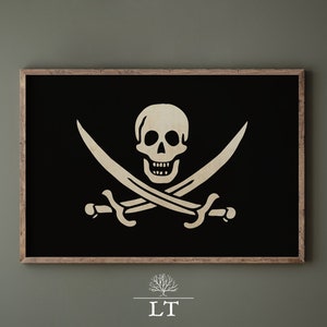 Op de afbeelding: Een zwart-witte ingelijste print van een piraten schedel en gekruiste beenderen. De schedel is wit met een zwarte oogkas en een zwarte glimlach. De gekruiste beenderen zijn wit en zijn gekruist achter de schedel.