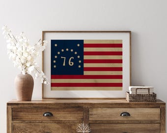 Peut inclure: Impression encadrée d'un drapeau américain vintage. Le drapeau présente un canton bleu avec 13 étoiles en cercle, le chiffre "76" au centre et des rayures rouges et beiges. L'impression est exposée sur une commode en bois.