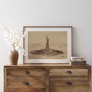May include: A framed sepia-toned print of the Statue of Liberty on a wooden dresser with two drawers. The print shows the statue on an island with a view of the city in the background.
