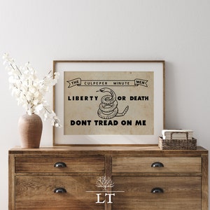 May include: A vintage-style print with a black and white image of a coiled rattlesnake with the text "The Culpeper Minute Men Liberty or Death Don't Tread On Me".