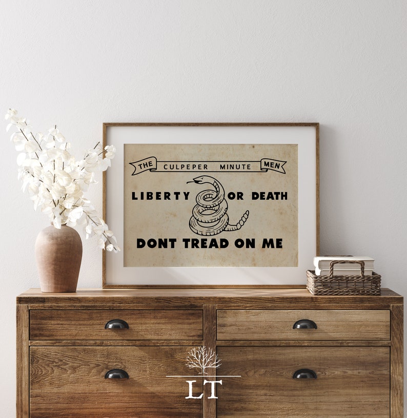May include: A vintage-style print with a black and white image of a coiled rattlesnake with the text "The Culpeper Minute Men Liberty or Death Don't Tread On Me".