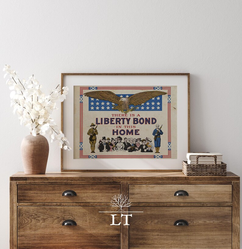 May include: Framed vintage Liberty Bond poster featuring an eagle with outstretched wings above the text "THERE IS A LIBERTY BOND IN THIS HOME." The poster has a red, white, and blue border and depicts soldiers and civilians.