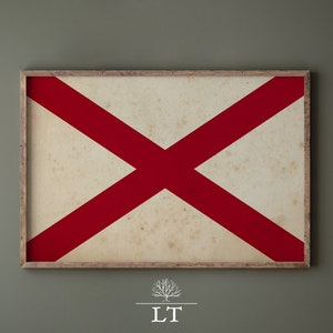 Puede incluir: Una impresi&oacute;n enmarcada de la bandera de Alabama. La bandera es blanca con una cruz roja en el centro. El marco es de madera y tiene un aspecto desgastado.