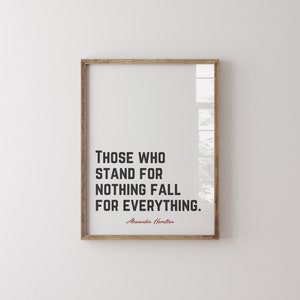 Może przedstawiać: Oprawiony wydruk z cytatem "CI, KTÓRZY NIE STOJĄ ZA NICZYM, UPADAJĄ ZA WSZYSTKO." w czarnym tekście. Imię autora, Alexander Hamilton, jest koloru czerwonego. Rama jest w kolorze jasnobrązowym.