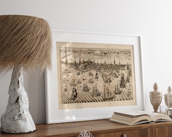 May include: A framed black and white vintage map of a city with ships and buildings. The map is in a white frame and is hanging on a white wall above a wooden cabinet.