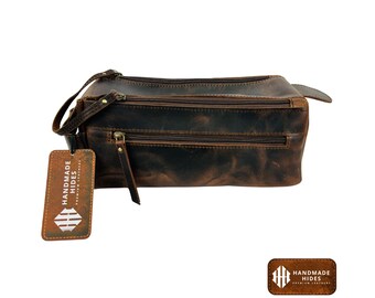 May include: A brown leather travel bag with two zippered compartments and a brown leather tag that says "Handmade Hides".