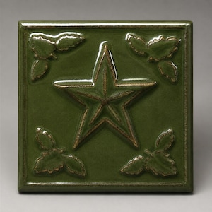 May include: A square, olive green ceramic tile featuring a raised, five-pointed star in the center. The tile is decorated with embossed leaf clusters in each of the four corners. The edges and raised details have a subtle, metallic bronze finish.