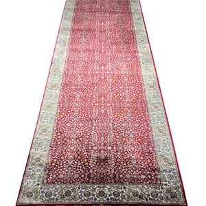 May include: A long, rectangular red rug with an intricate floral pattern. The rug has a cream-colored border with green and gold accents. The edges are finished with a dark red border and white fringe.