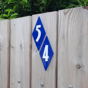 May include: A wooden fence with a blue diamond-shaped house number sign that reads "54".