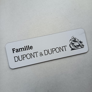Könnte beinhalten: Ein weißes rechteckiges Namensschild mit abgerundeten Ecken. Der Text "Famille DUPONT & DUPONT" ist in Schwarz gedruckt, zusammen mit einer schwarzen Grafik eines Motorrads und Fahrers.