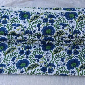 May include: A folded fabric with a white background and a blue floral pattern. The fabric has a green and yellow floral design.