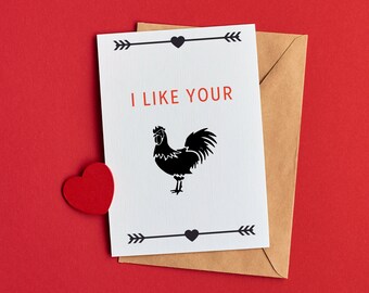 May include: A greeting card with the text "I LIKE YOUR" in red, and a black rooster illustration. The card is on a brown envelope, with a red heart on a red background.