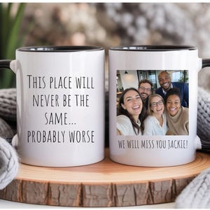 May include: Two white ceramic mugs with black handles and rims. One mug features the black text: This place will never be the same... probably worse. The other mug displays a colour photograph of five people and the text: We will miss you Jackie!