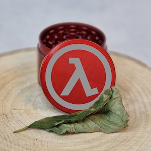 Può includere: Un macinino in metallo rosso con un simbolo Lambda bianco sul coperchio. Il macinino è su una superficie di legno.