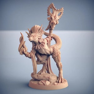 May include: A miniature figurine of a lizard-like creature with a staff and a flame in its hand. The creature is wearing a decorative headdress and a cloak. The figurine is made of a light brown plastic.