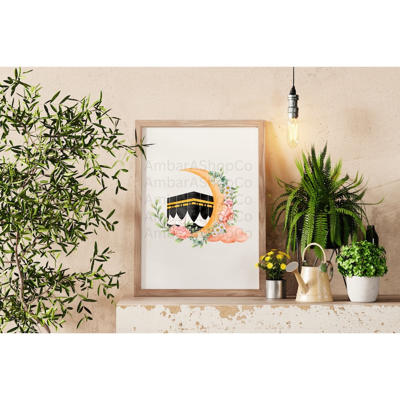 May include: A watercolor print of the Kaaba, the holiest site in Islam, with a crescent moon and flowers. The print is framed in a wooden frame and is ready to hang on a wall.