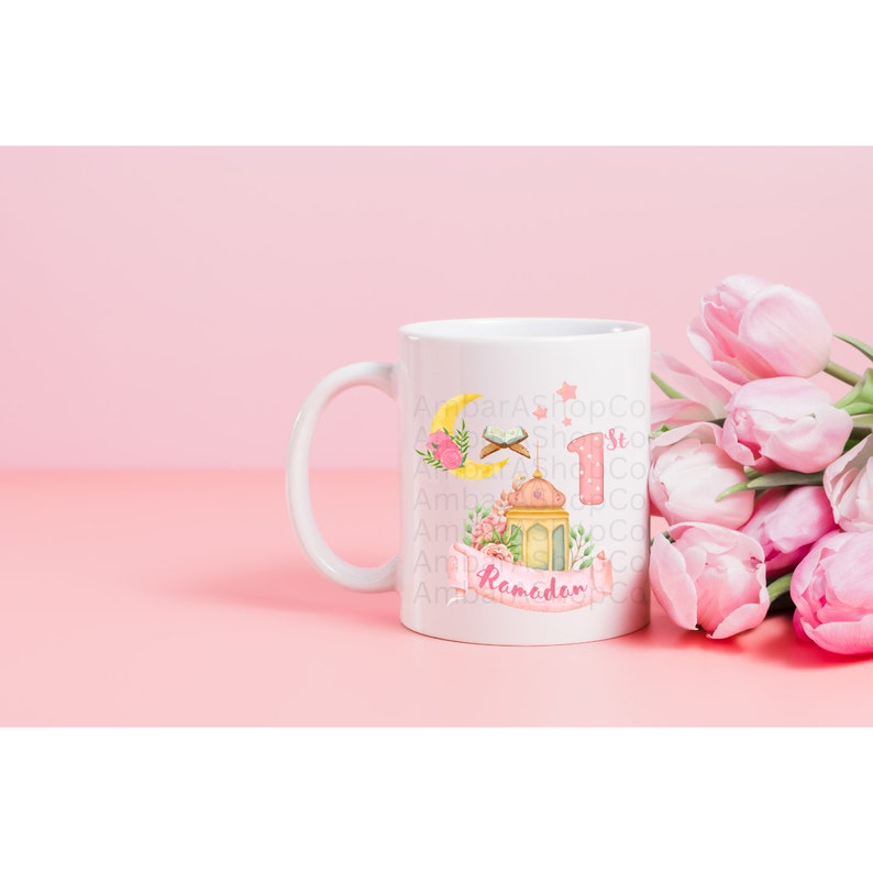 May include: White ceramic mug with a pink and yellow Ramadan design. The design features a crescent moon, a mosque, a lantern, and the words "1st Ramadan".