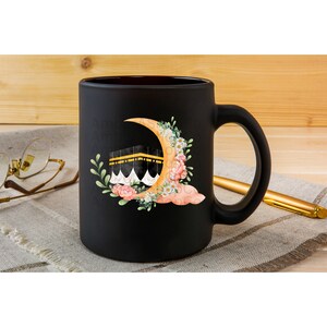 May include: Black ceramic coffee mug with a white crescent moon and a gold building with a white dome. The moon is surrounded by pink and white flowers and green leaves.