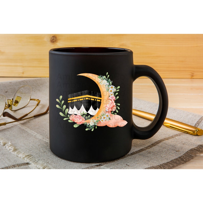 May include: Black ceramic coffee mug with a white crescent moon and a gold building with a white dome. The moon is surrounded by pink and white flowers and green leaves.