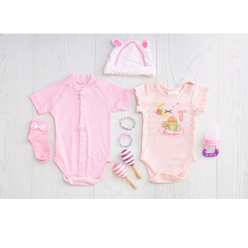 May include: Pink baby clothes set with a pink hat, two pink bodysuits, a pair of pink socks, a set of colorful bracelets, and a pink and purple maraca. One bodysuit has a Ramadan design with the text "Ramadan".