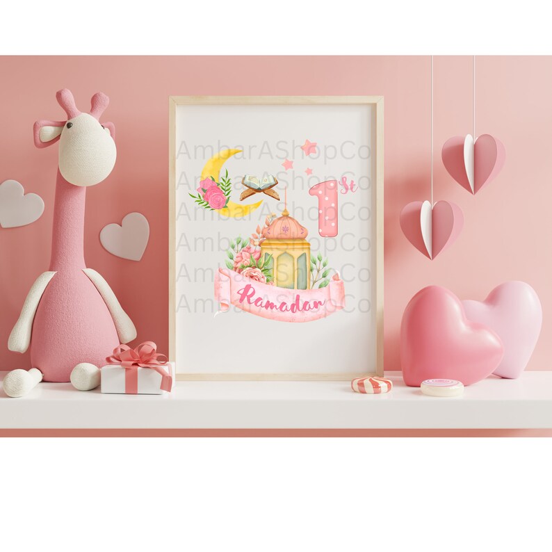 May include: A pink and yellow Ramadan themed printable with a crescent moon, a lantern, a prayer rug, and the number 1. The text "Ramadan" is on a pink ribbon.
