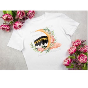 May include: White t-shirt with a watercolor illustration of a crescent moon with a floral design and a black and white image of the Kaaba. The text "AmbarAShopCo" is repeated in the background.