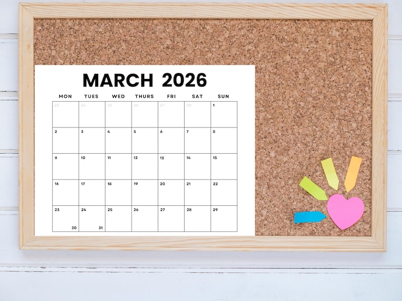 Pode incluir: Um quadro de corti&ccedil;a com um calend&aacute;rio para mar&ccedil;o de 2026. O calend&aacute;rio &eacute; impresso em papel branco e tem uma borda preta. H&aacute; notas adesivas coloridas e um cora&ccedil;&atilde;o rosa no quadro de corti&ccedil;a.
