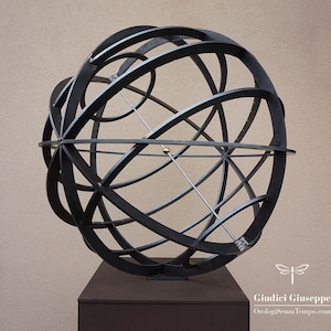 Puede incluir: Una escultura de metal negro de una esfera con intrincados diseños geométricos. La esfera está montada sobre una base cuadrada.