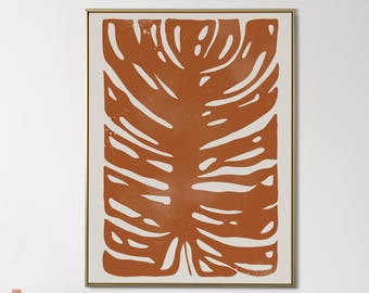 May include: A framed art print featuring a large, stylized illustration of a monstera leaf in shades of orange and cream. The leaf design has a textured appearance and is set against a cream background, framed in a gold tone.