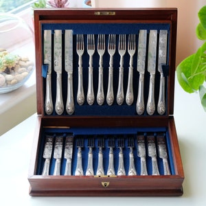 May include: A wooden box with a blue velvet interior containing a set of silver cutlery. The cutlery includes forks and knives with ornate handles.
