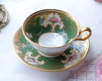May include: A vintage teacup and saucer set. The teacup and saucer are green with gold trim and floral accents. The teacup has a white interior and a gold handle. The saucer has a matching design. A classic tea set.