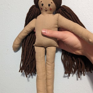 May include: A handmade rag doll with brown yarn hair, a beige fabric body, and a stitched face with brown eyes and red cheeks.
