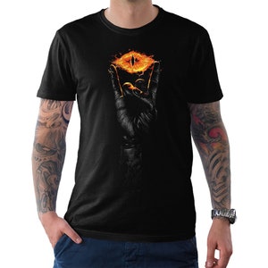 May include: Black t-shirt featuring a graphic of a hand holding a fiery eye. The eye is orange and yellow with black pupils. The hand is black and the background is black.