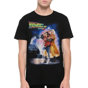 Może przedstawiać: Czarny T-shirt z grafiką Marty'ego McFly'a i Doktora Emmetta Browna z filmu Powrót do przyszłości II. Grafika przedstawia ich stojących przed DeLoreanem, wehikułem czasu.