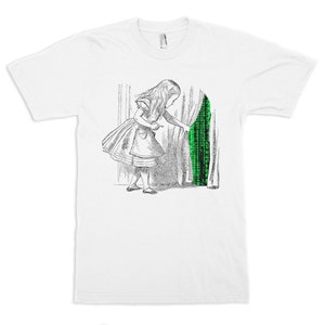 May include: A white t-shirt with a black and white illustration of a girl in a dress peeking behind a curtain. The curtain reveals a green matrix-like code.