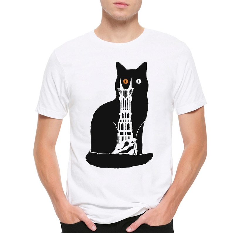 Puede incluir: Camiseta blanca con una silueta negra de un gato con un ojo naranja. El gato sostiene una torre en sus patas.