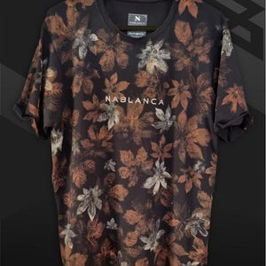 May include: Black t-shirt with a brown and white leaf print. The shirt has the text "NABLANCA" printed on the front.