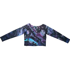 Op de afbeelding: Een shirt met lange mouwen en tie-dye in tinten zwart, paars en blauw. Het shirt heeft een V-hals en een cropped pasvorm. Het tie-dye patroon creëert een gemarmerd effect over de stof.