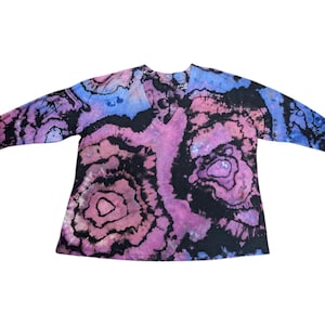 Op de afbeelding: Een shirt met lange mouwen en een V-hals met een tie-dye patroon in roze, blauwe en zwarte tinten.
