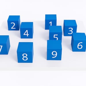 May include: Nine blue cubes with white numbers from one to nine are arranged on a white rectangular surface. The cubes are evenly spaced and the numbers are clearly visible, making it a learning tool.