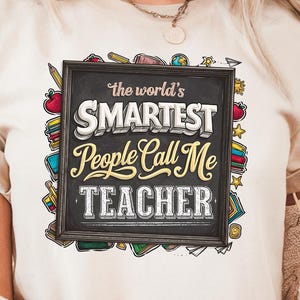 May include: Beige t-shirt with rolled sleeves featuring the text "the world's SMARTEST People Call Me TEACHER" in a chalkboard-style design. The graphic includes colourful school-themed illustrations. The shirt is worn by a person.