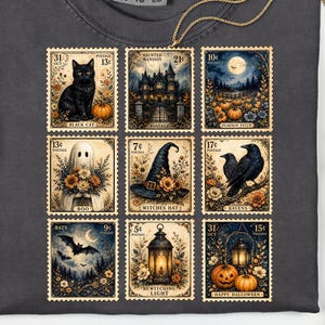 May include: A charcoal grey t-shirt featuring a grid of nine vintage-style postage stamp illustrations. The designs include a black cat, a haunted mansion, a pumpkin patch, a ghost, a witch's hat, ravens, bats, a lantern, and jack-o'-lanterns.